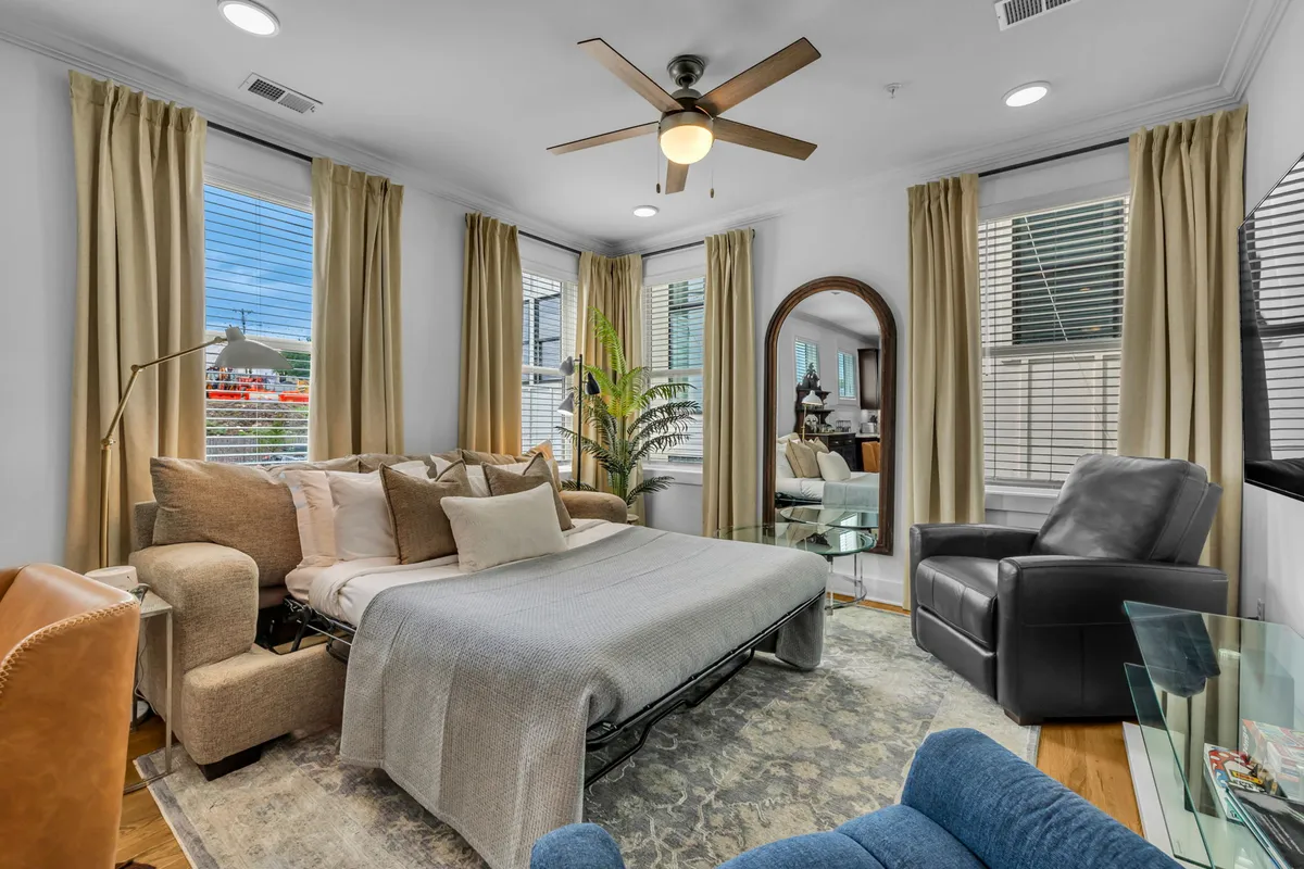 A comfortable living area is shown, anchored by a plush sofa bed, armchair, large mirror, and window views. There's a sense of daylight and welcoming ambiance, suited for both relaxation and social connection, as described in the section.