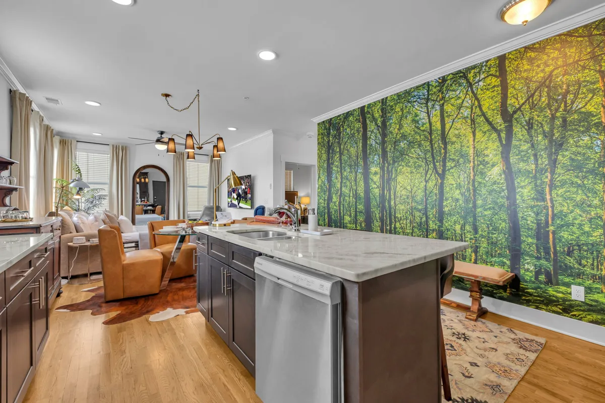 Bright, modern kitchen and living area with a striking forest mural along one wall, comfortable seating, and a welcoming atmosphere. Large windows offer natural light and a view of the outdoors, blending interior style with inspiration from the local environment.