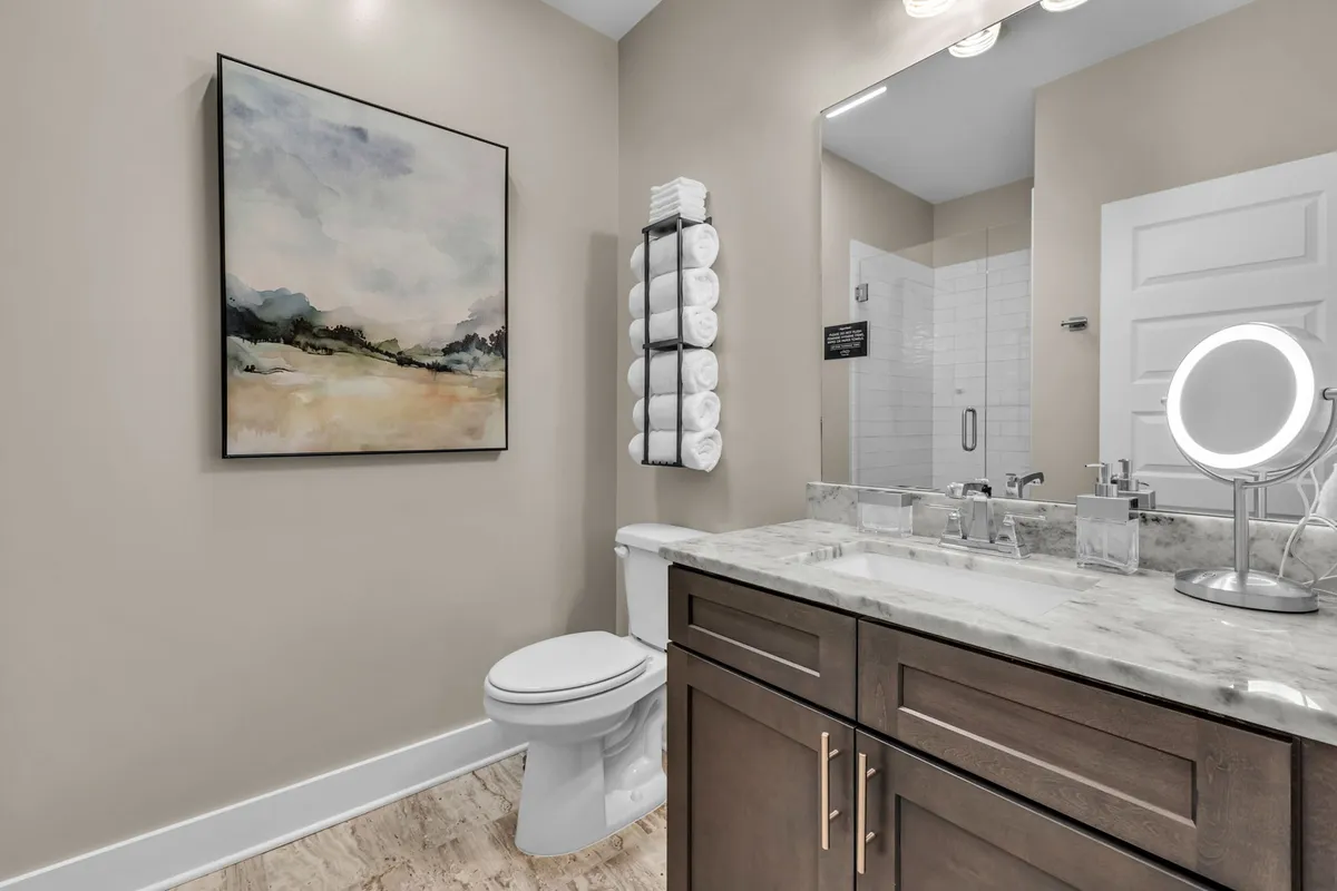 A modern bathroom with a sleek vanity, elegant mirror, fluffy towels, and a framed painting on the wall. The ambiance is calm and spa-like, suggesting both relaxation and functionality for personal care routines.