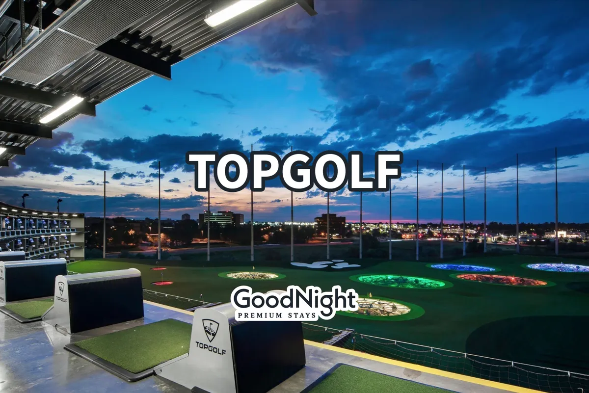 A lively exterior shot of Topgolf's driving range, featuring colorful targets under a vibrant sky. Groups of people are seen enjoying golfing, socializing, and catching sunset views, with the city atmosphere buzzing in the background.