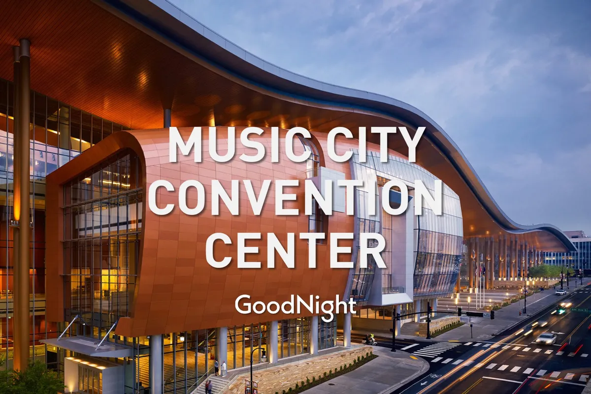 A striking exterior view of the Music City Center, characterized by its distinctive curved architecture and illuminated signage. The expansive glass facade hints at major conferences, exhibitions, and networking opportunities nearby.