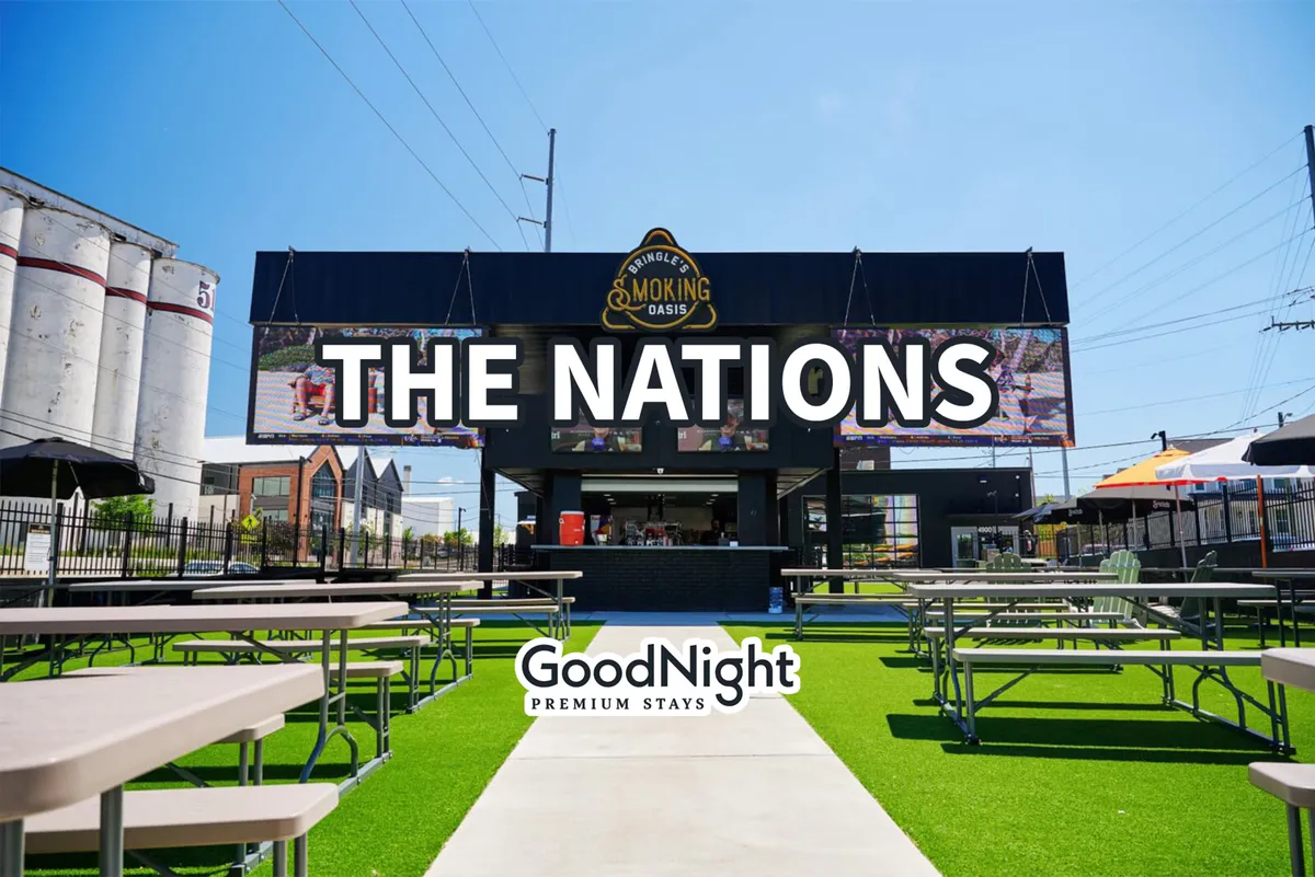 A vibrant exterior view of a lively dining area in West Nashville, featuring a large sign reading 'THE NATIONS', outdoor seating, food and drink service, and green artificial grass. The mood is social and festive, highlighting the area's unique dining and community events.