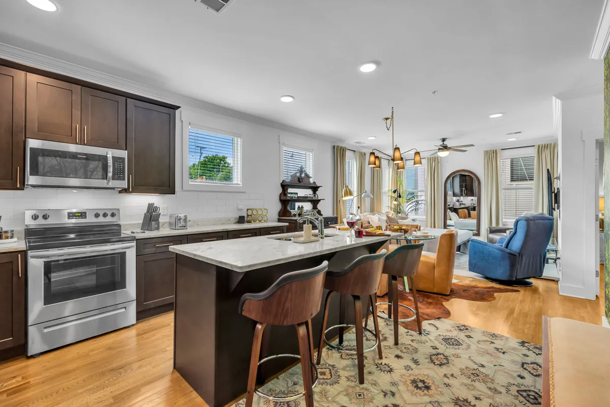 The image showcases a stylish, open-concept living space featuring a modern kitchen island with sleek stainless steel appliances, a cozy dining area perfect for intimate meals, and a comfortable living area anchored by a striking blue chair. The space exudes warmth, with inviting lighting and thoughtful design touches that create a welcoming atmosphere ideal for relaxing or entertaining guests.